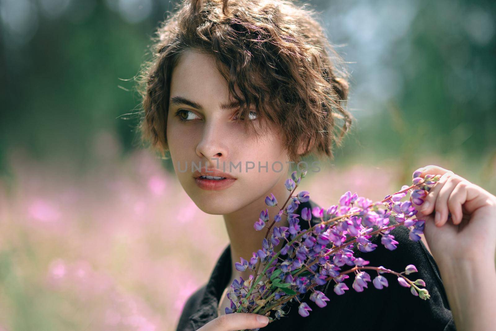 Young woman with a bouquet of lupines in her hand against the background of blooming Ivan-tea A meadow with purple flowers in summer.