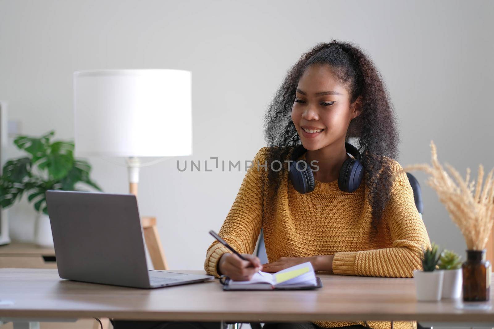 Young adult happy smiling Hispanic Asian student wearing headphones talking on online chat meeting using laptop in university campus or at virtual office. College female student learning remotely. by wichayada