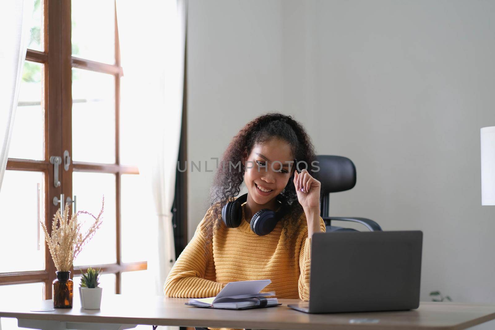 Young adult happy smiling Hispanic Asian student wearing headphones talking on online chat meeting using laptop in university campus or at virtual office. College female student learning remotely..