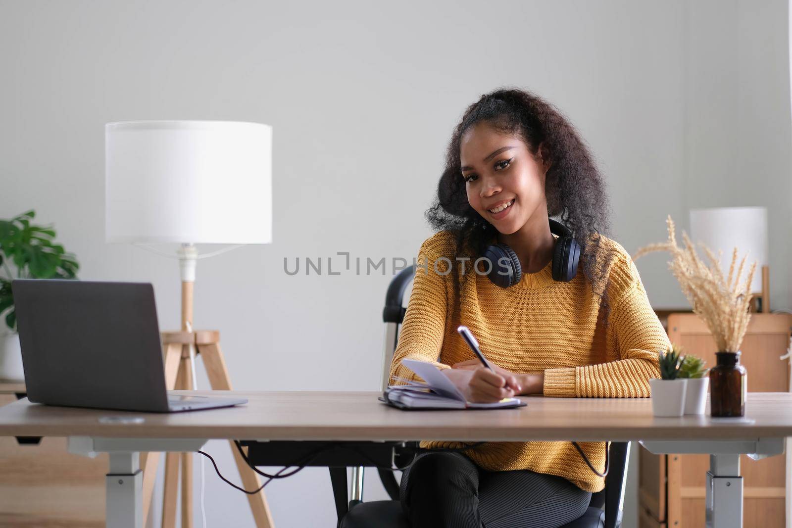 Young adult happy smiling Hispanic Asian student wearing headphones talking on online chat meeting using laptop in university campus or at virtual office. College female student learning remotely. by wichayada