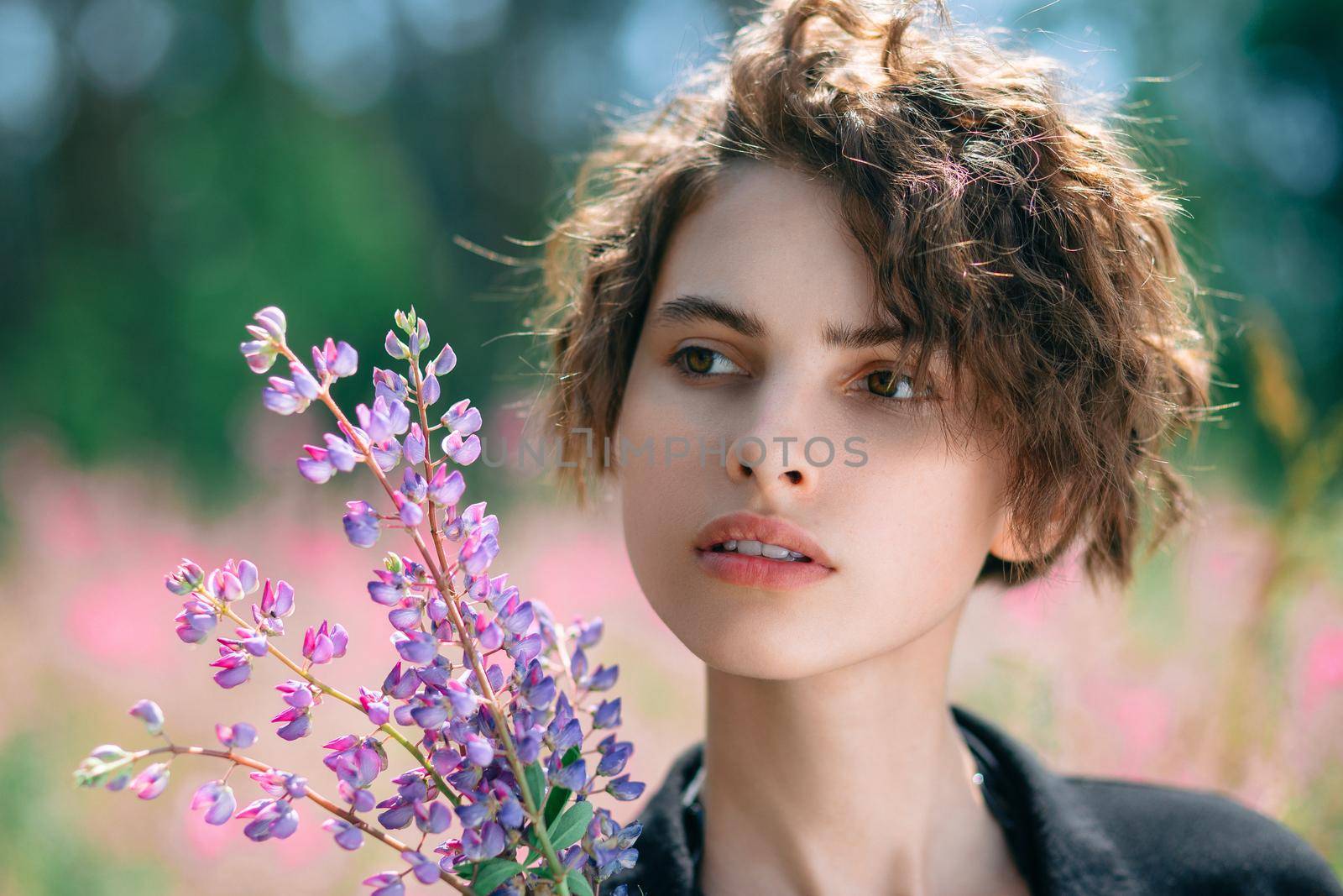 Beautiful young woman with a bouquet of lupines in her hand. Soft focus. Close-up