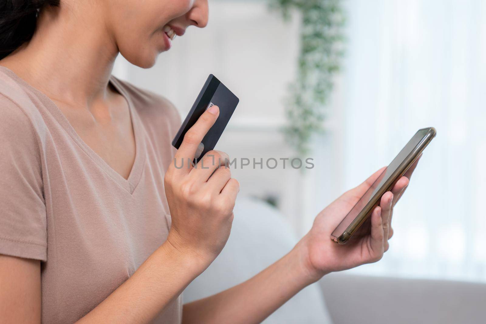Contented young woman eagerly makes an online purchase using her smartphone. by biancoblue