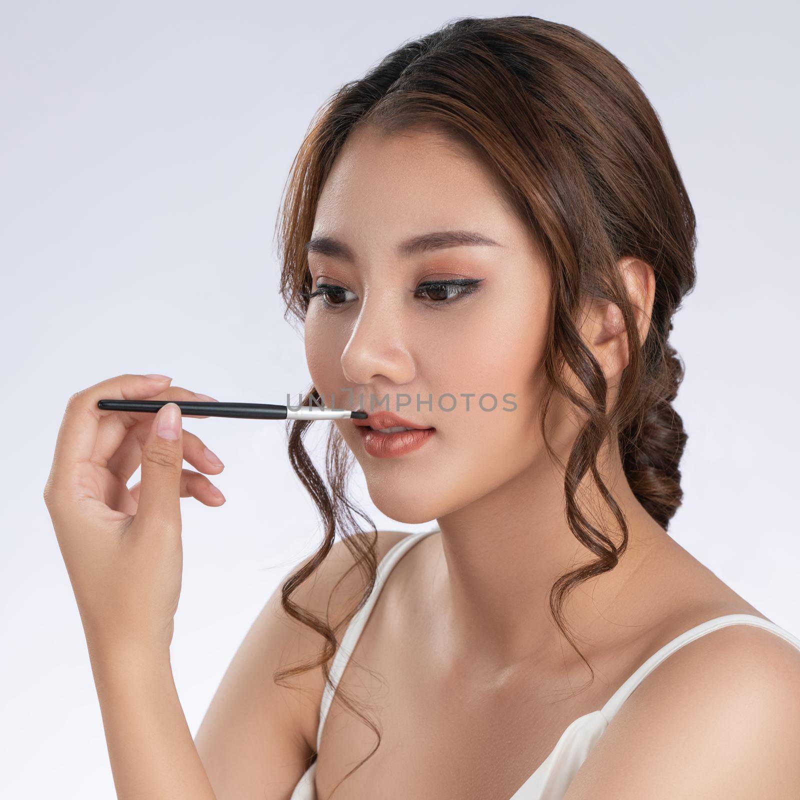 Closeup portrait of young gorgeous woman with healthy fair skin applying lipstick on her lip while looking at camera. Beauty concept with cosmetic and makeup.