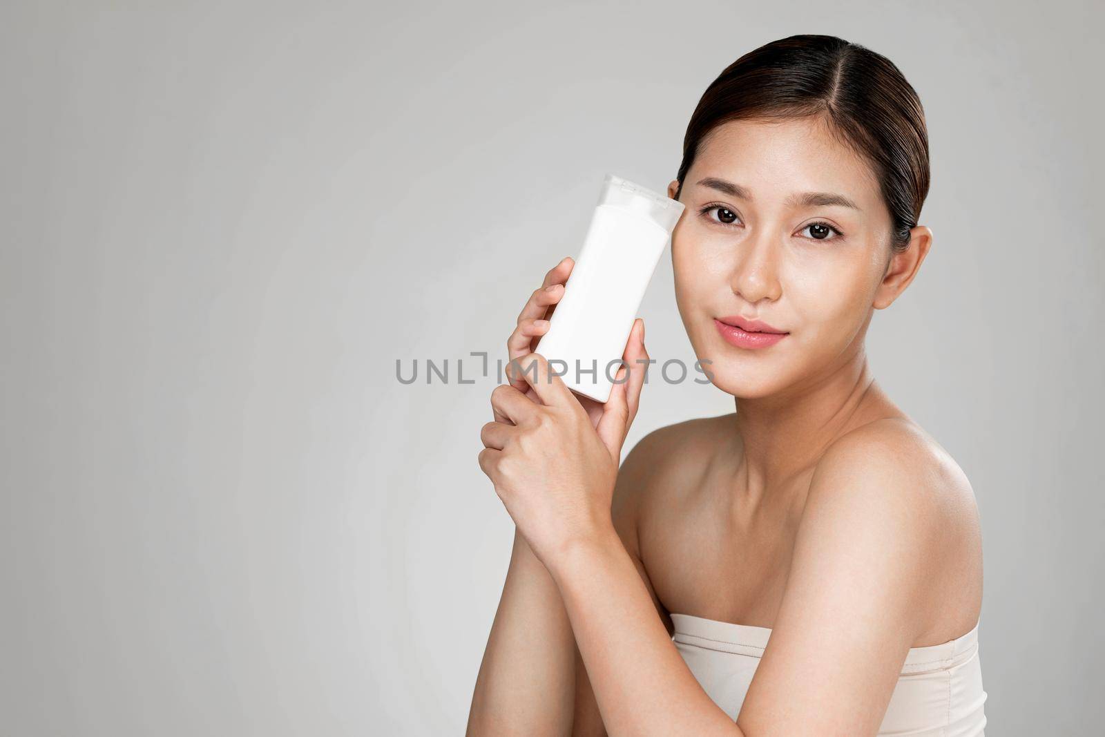 Ardent woman smiling holding mockup product for advertising text place, light grey background. Concept of healthcare for skin, beauty care product for advertising.