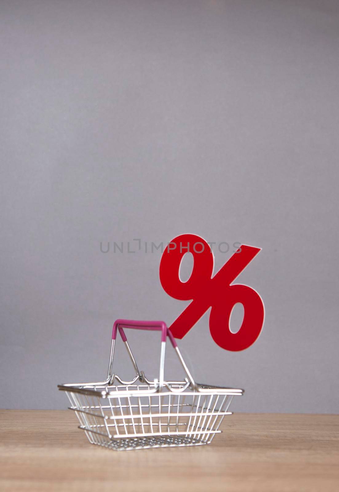 Shopping cart from the supermarket with sign percent over gray paper wall background. Shopping in the Mall, shop, shopping, a large selection.
