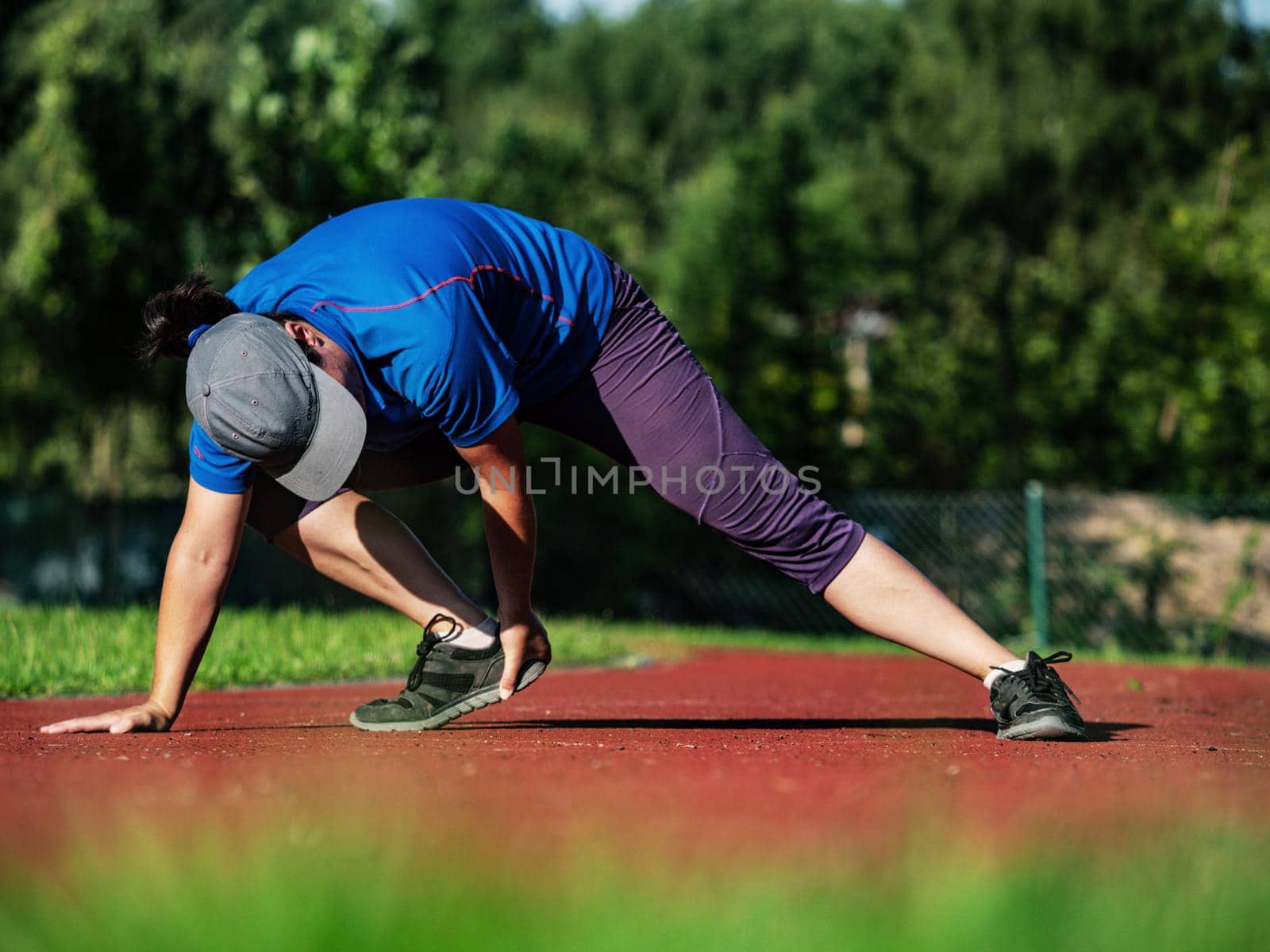 Middle age woman stretching legs and body before run during sunny morning on stadium 