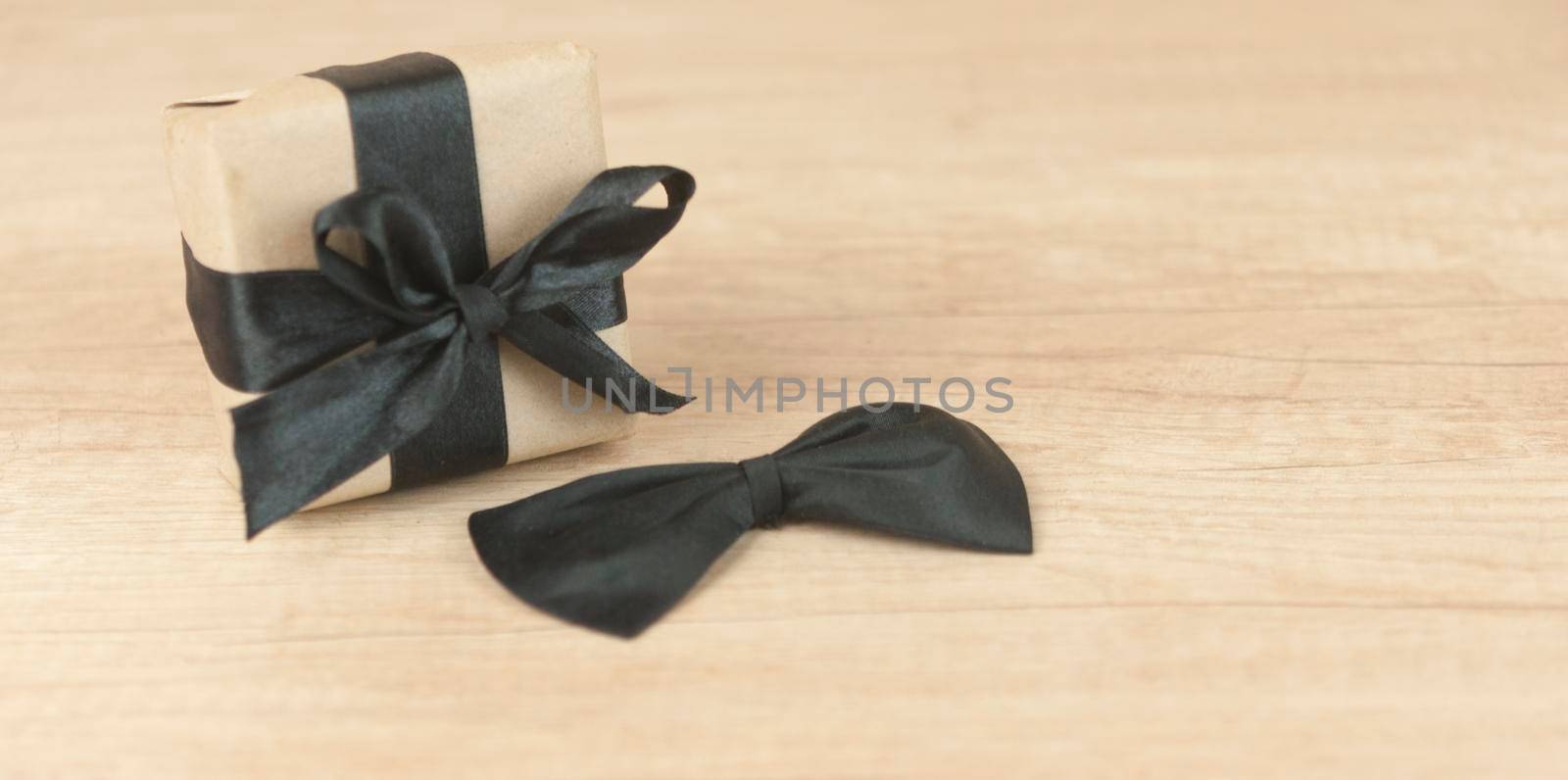 One gift box wrapped in craft paper and tied with bow on wood background. Concept Father's Day or Birthday background. Top view. International men's day concept. by inxti