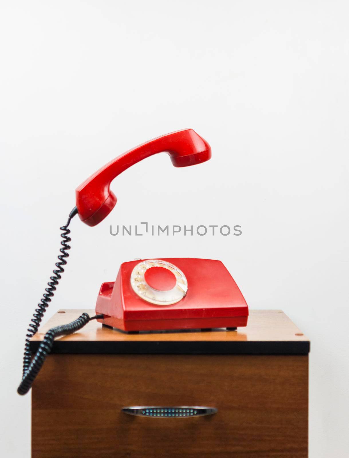 Urgent call waiting , classic red telephone receiver, old telephone on white background, flying in weightlessness with wooden desktop.