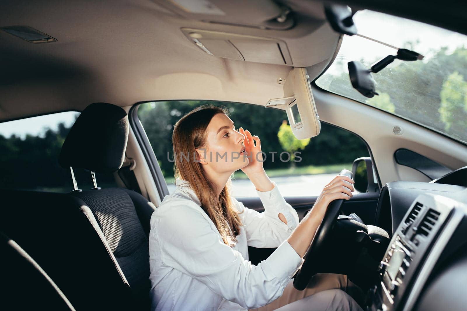 Beautiful woman watermelon in the car corrects makeup looking in the mirror before the trip