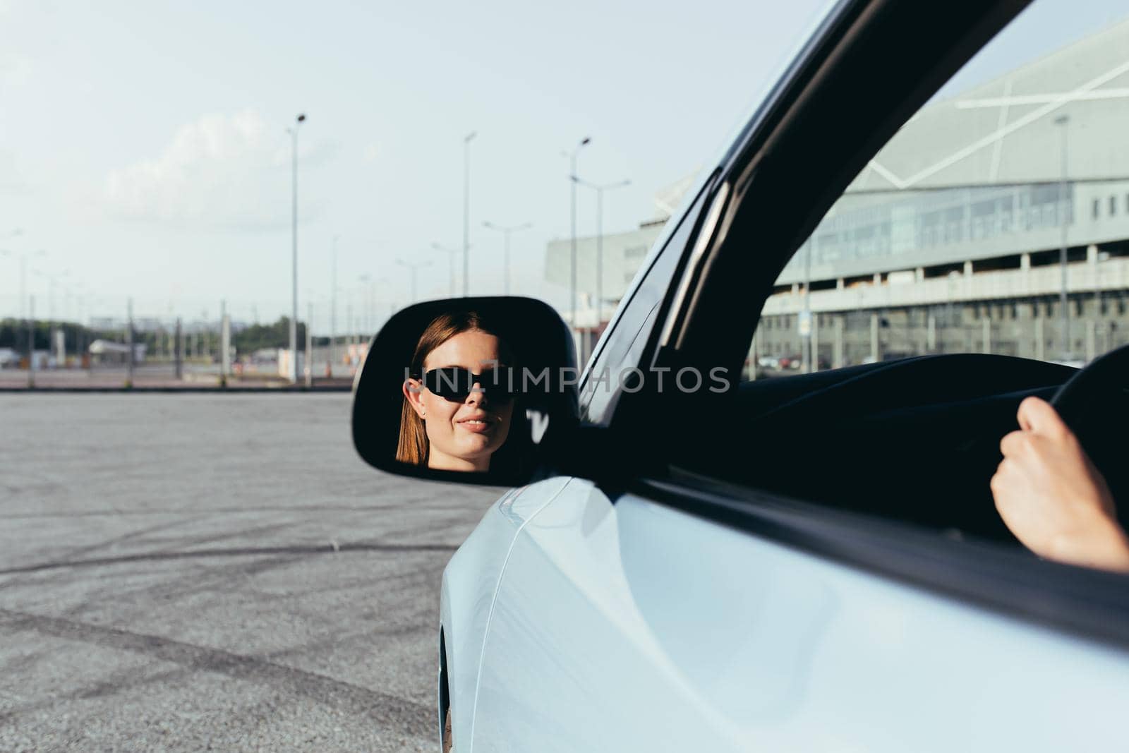 The woman is sitting in the car, beating in the side mirror, successful and joyful