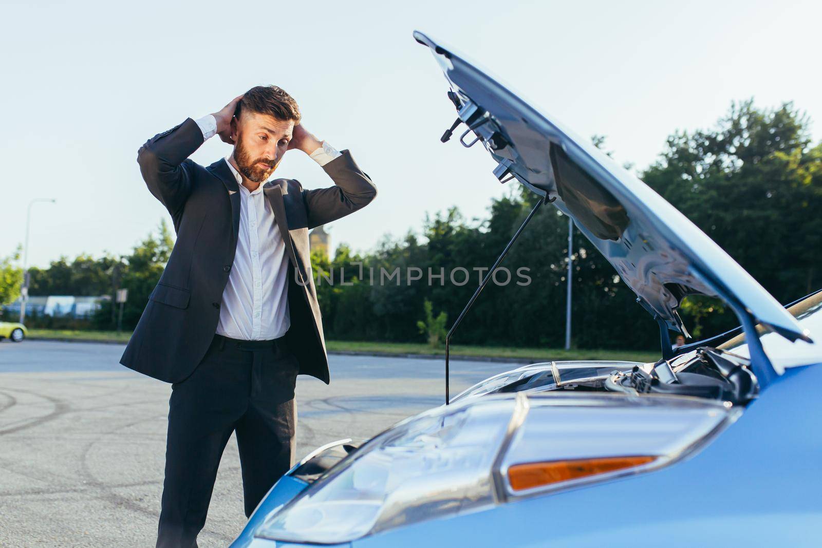 an annoyed and angry man, near a broken car, tries to call an insurance agent and a repair crew. for car repair