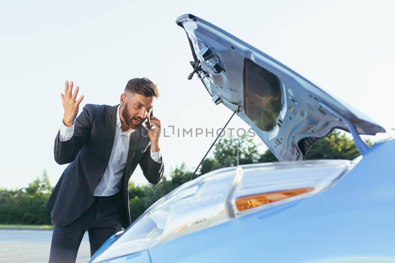 an annoyed and angry man, near a broken car, tries to call an insurance agent and a repair crew. for car repair
