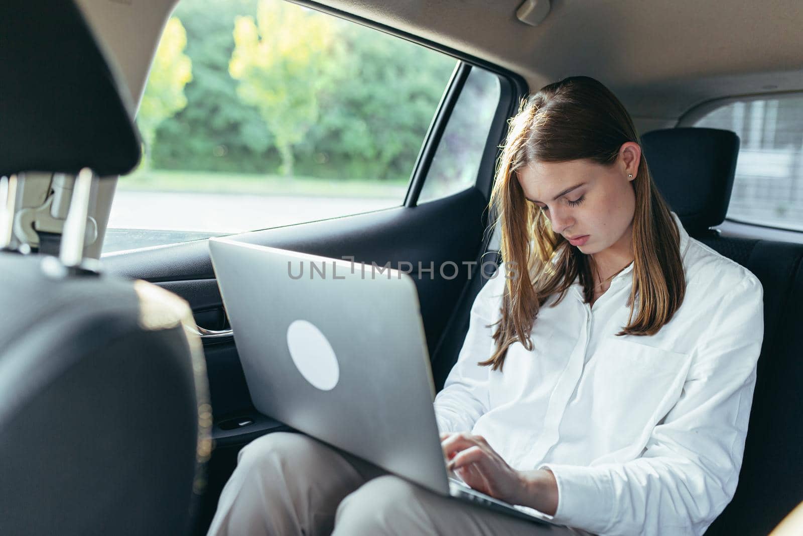 Tired female car passenger holding laptop in hands