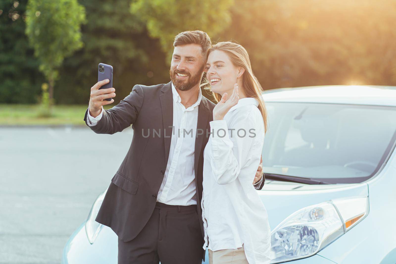 Young beautiful couple man and woman, happy to buy a new car, take photos together on the phone, and show friends shopping by video call by voronaman
