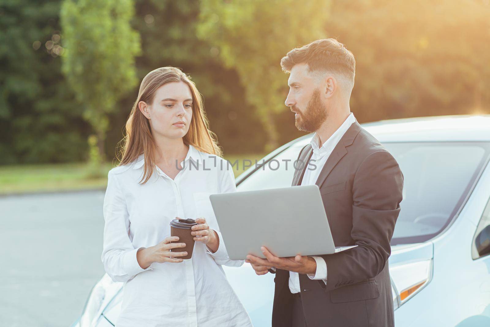 Male car salesman, recommends a car to a woman buyer, inspects cars in the showroom, the seller uses a laptop to view technical information on the car
