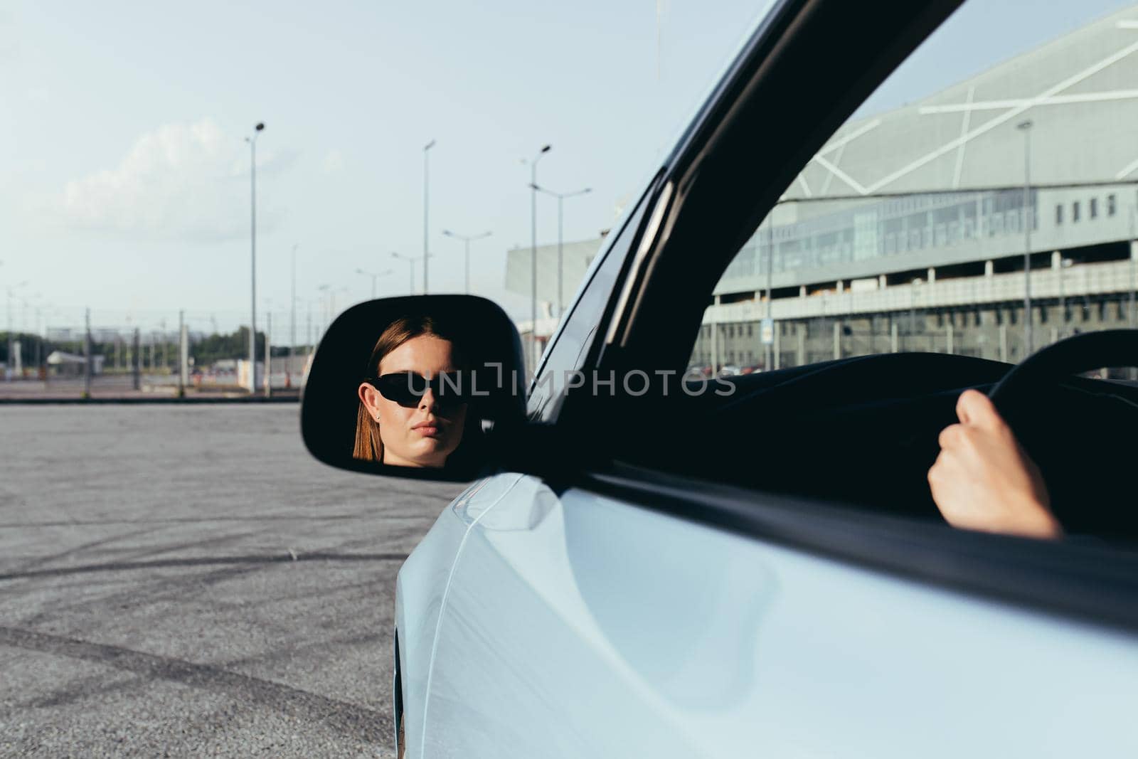 The woman is sitting in the car, beating in the side mirror, successful and joyful