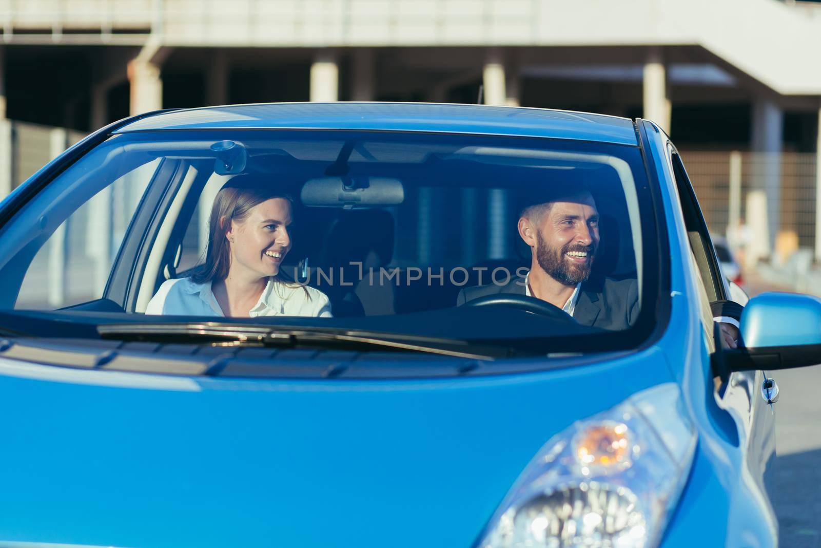 Male driving instructor and female driving school student sitting together in car smiling, learning to drive a car
