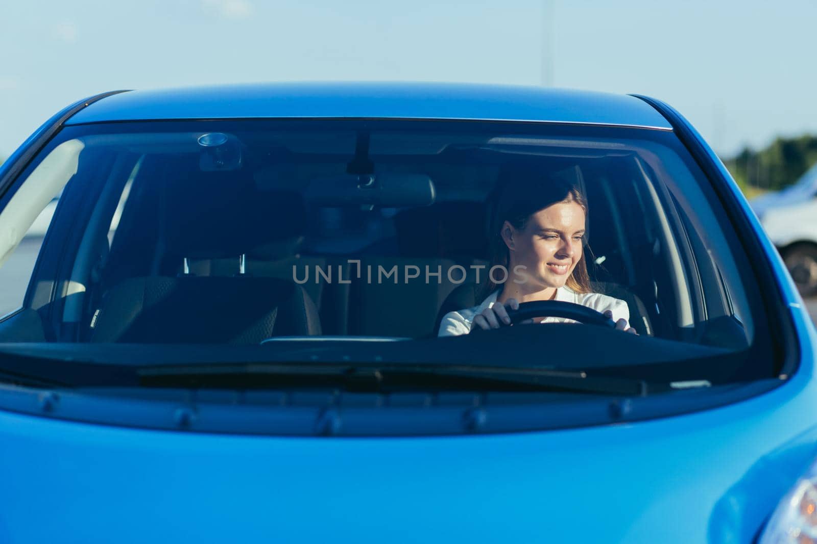 portrait of a successful and happy woman driving a car, photo from the front through the glass