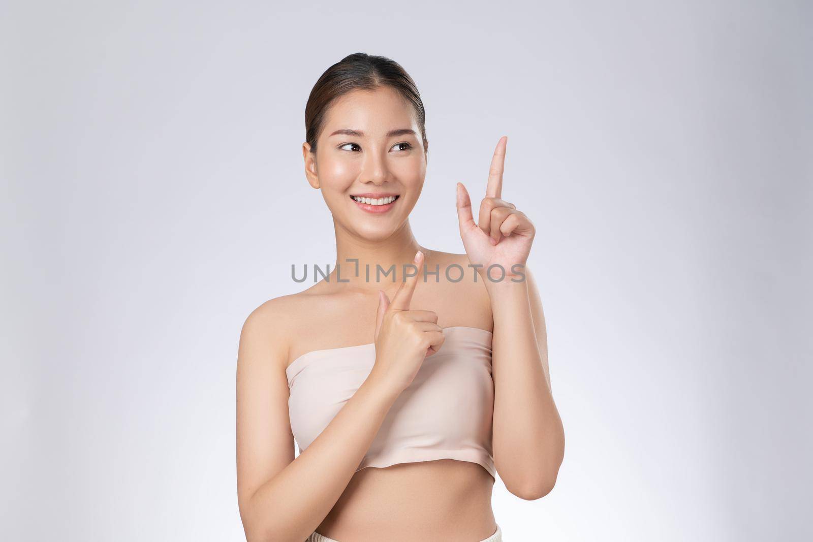 Photo of a gorgeous woman in a concept of empty space for beauty care product on isolated light gray background. Skincare product, model uses hand to create empty space for commercial.
