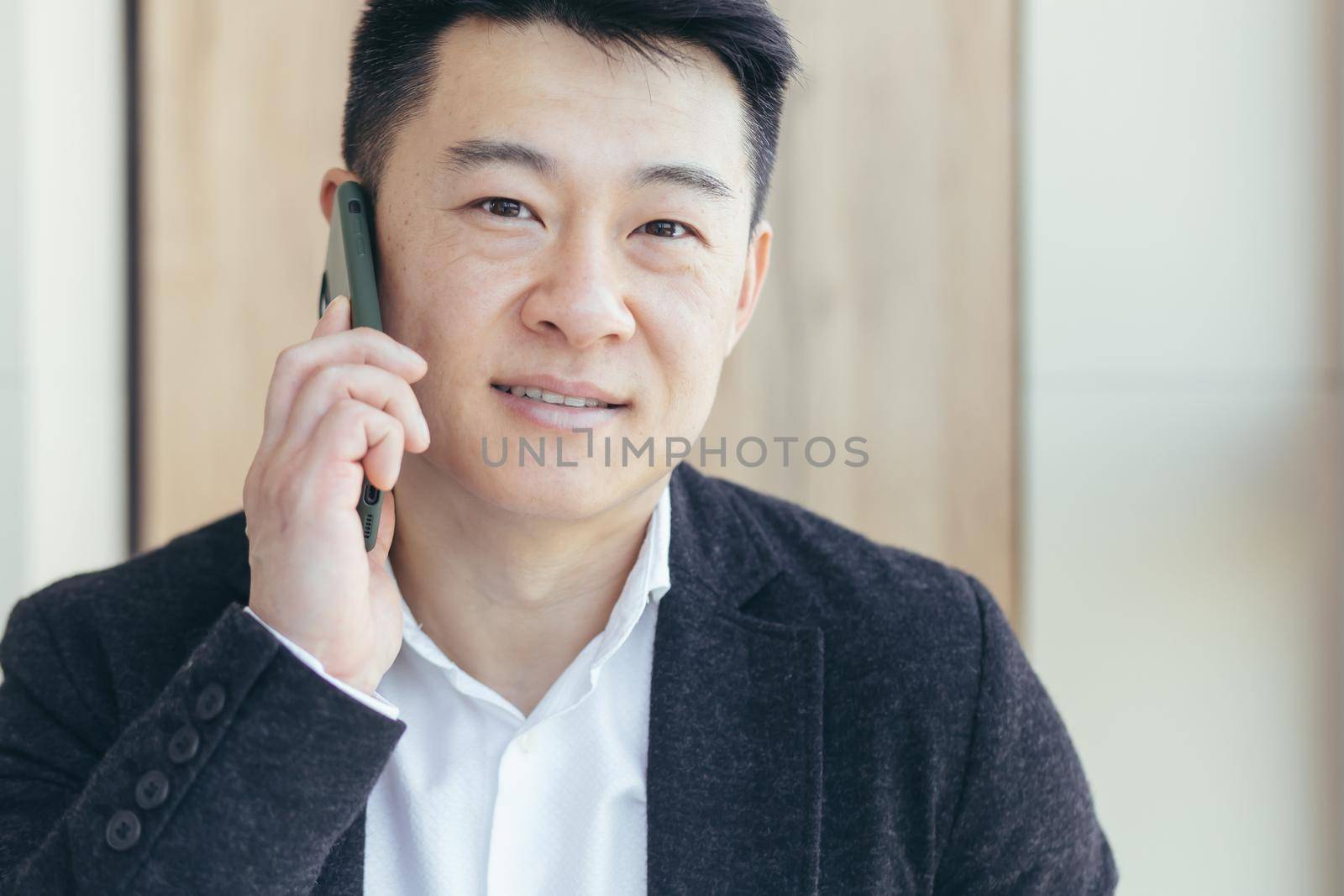 Asian businessman close-up portrait, successful and happy smiling talking on the phone, in a business suit