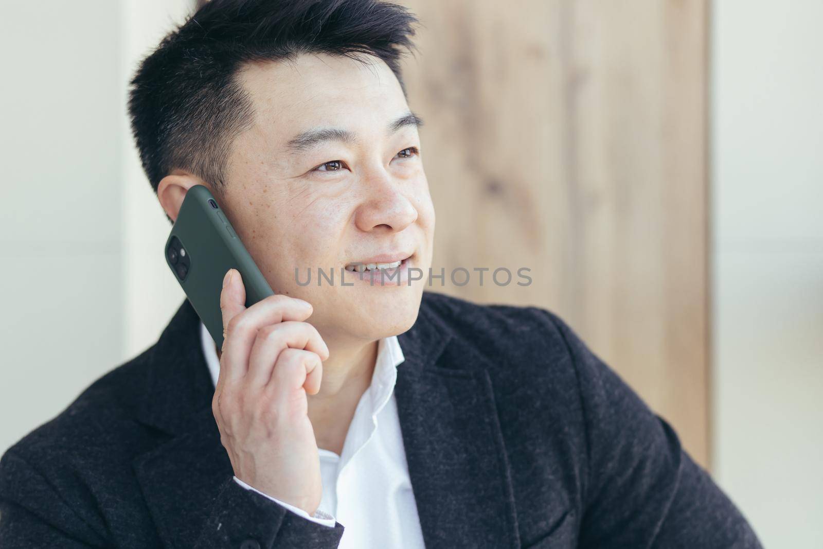 Asian businessman close-up portrait, successful and happy smiling talking on the phone, in a business suit