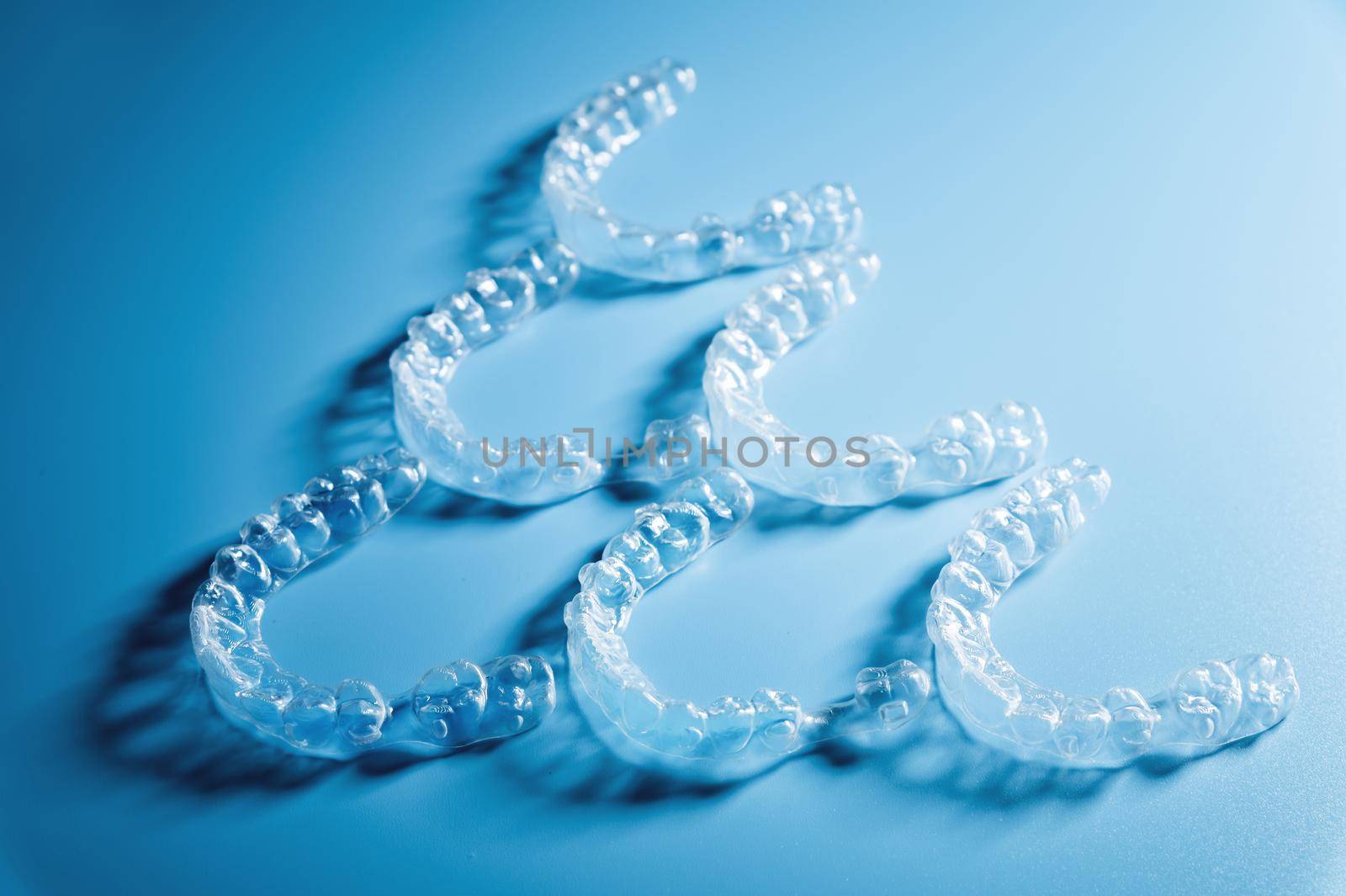 invisible plastic braces lie in a pyramid shape in a row on a blue background, studio shot, nobody.