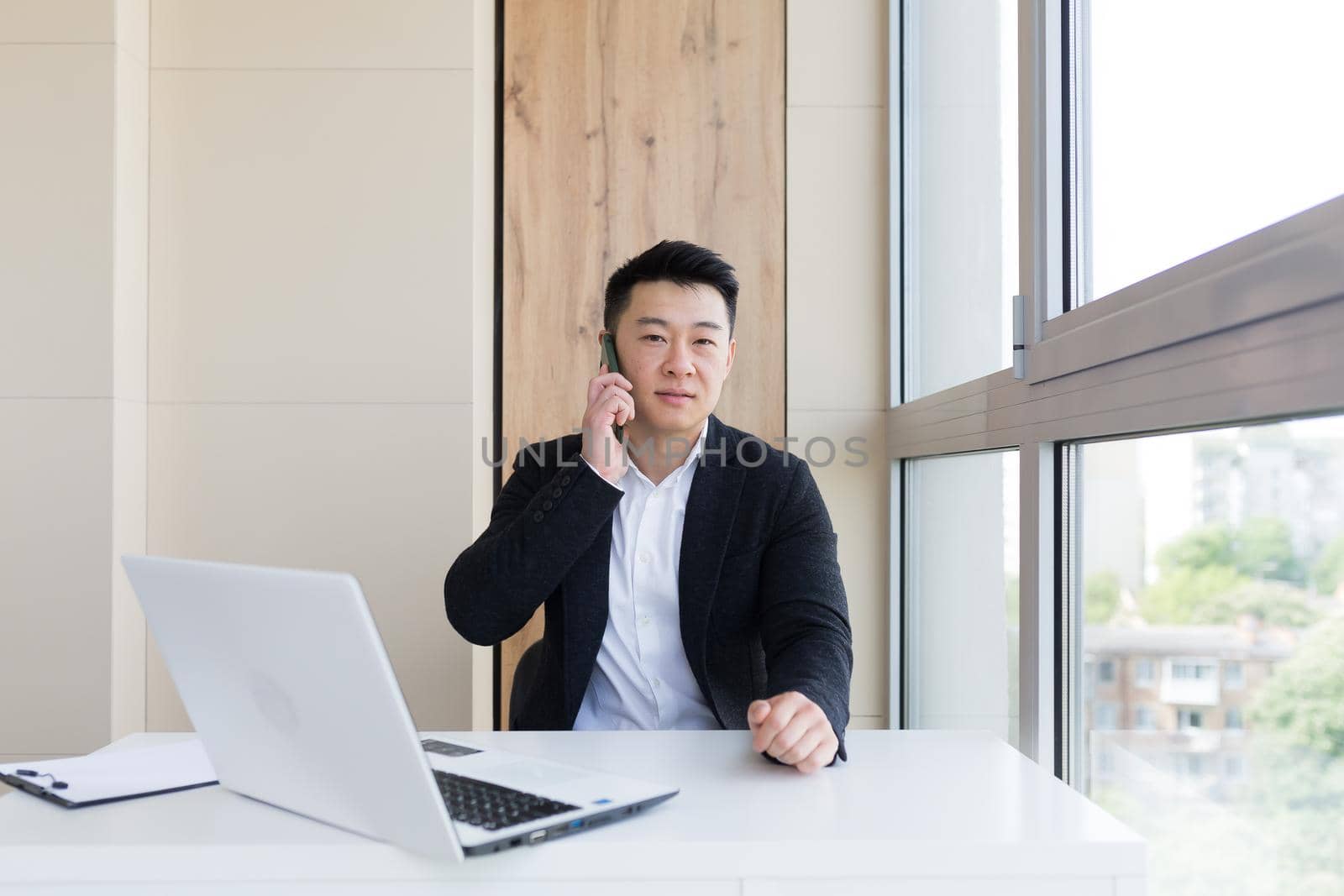 Serious asian business businessman uses cellphone to communicate with colleagues while sitting in modern office