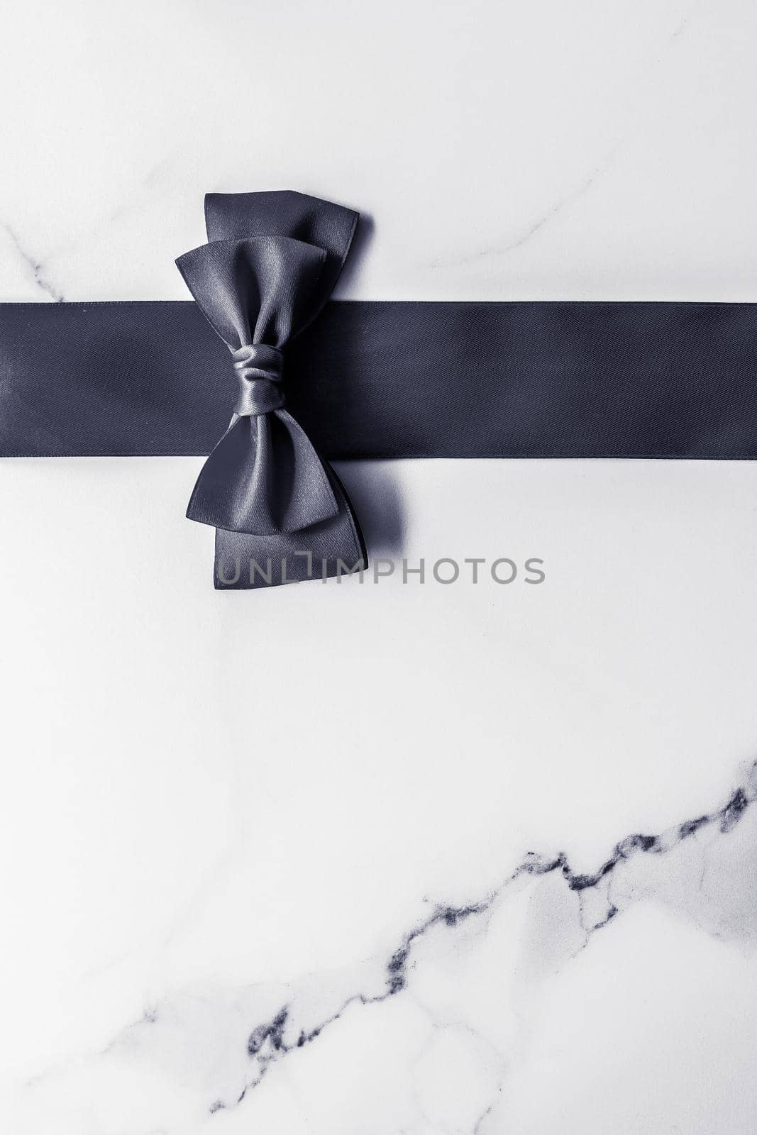 Black silk ribbon and bow on marble background, flatlay by Anneleven