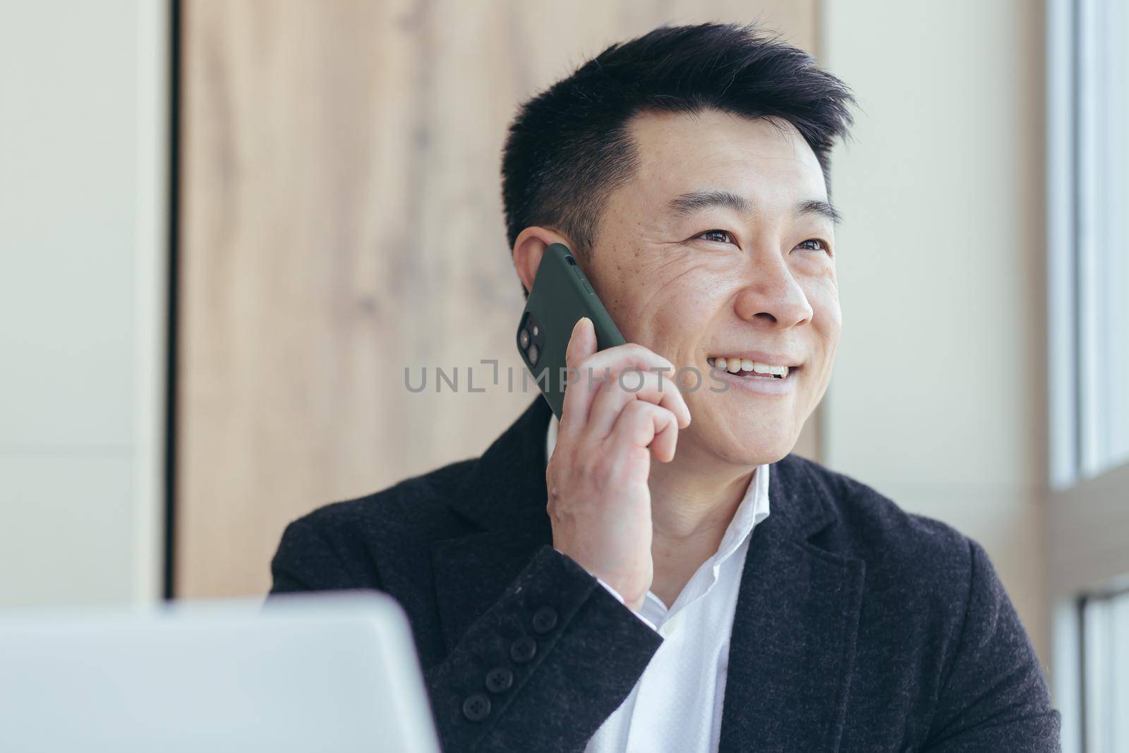 Asian businessman close-up portrait, successful and happy smiling talking on the phone, in a business suit by voronaman