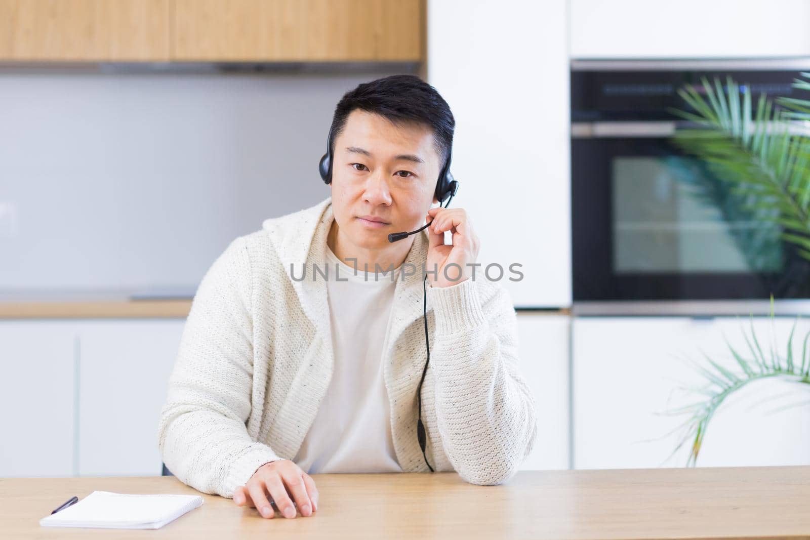 Asian man talking online on video call at home room with headset. Male in casual clothes looking at camera, meeting or conference in distance. Portrait student or teacher Lecture training. Webcam view