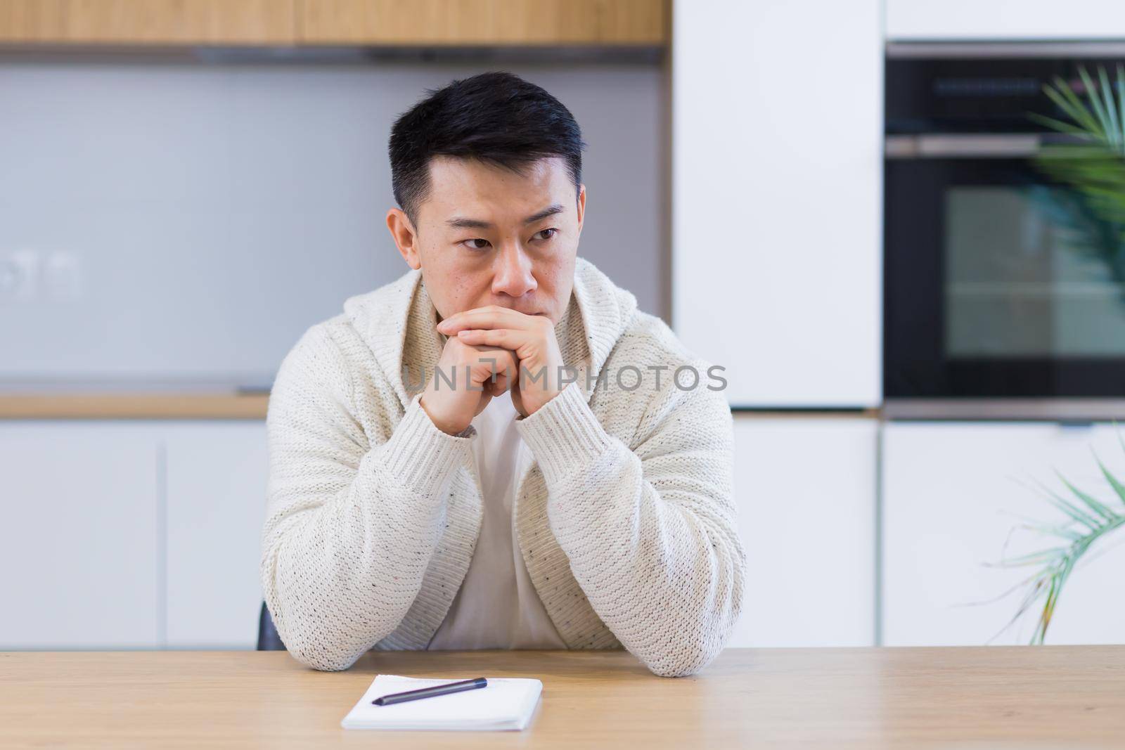 Thoughtful serious young asian man looking away. student writer sit at home office desk with laptop thinking of inspiration search solution ideas lost in thoughts dreaming solving financial problems
