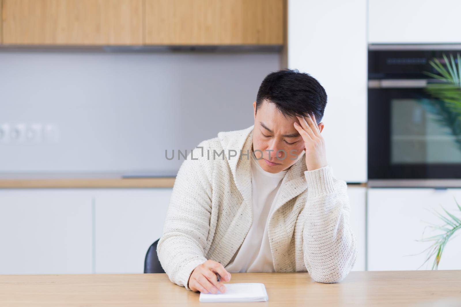 Thoughtful serious young asian man looking away. student writer sit at home office desk with laptop thinking of inspiration search solution ideas lost in thoughts dreaming solving financial problems