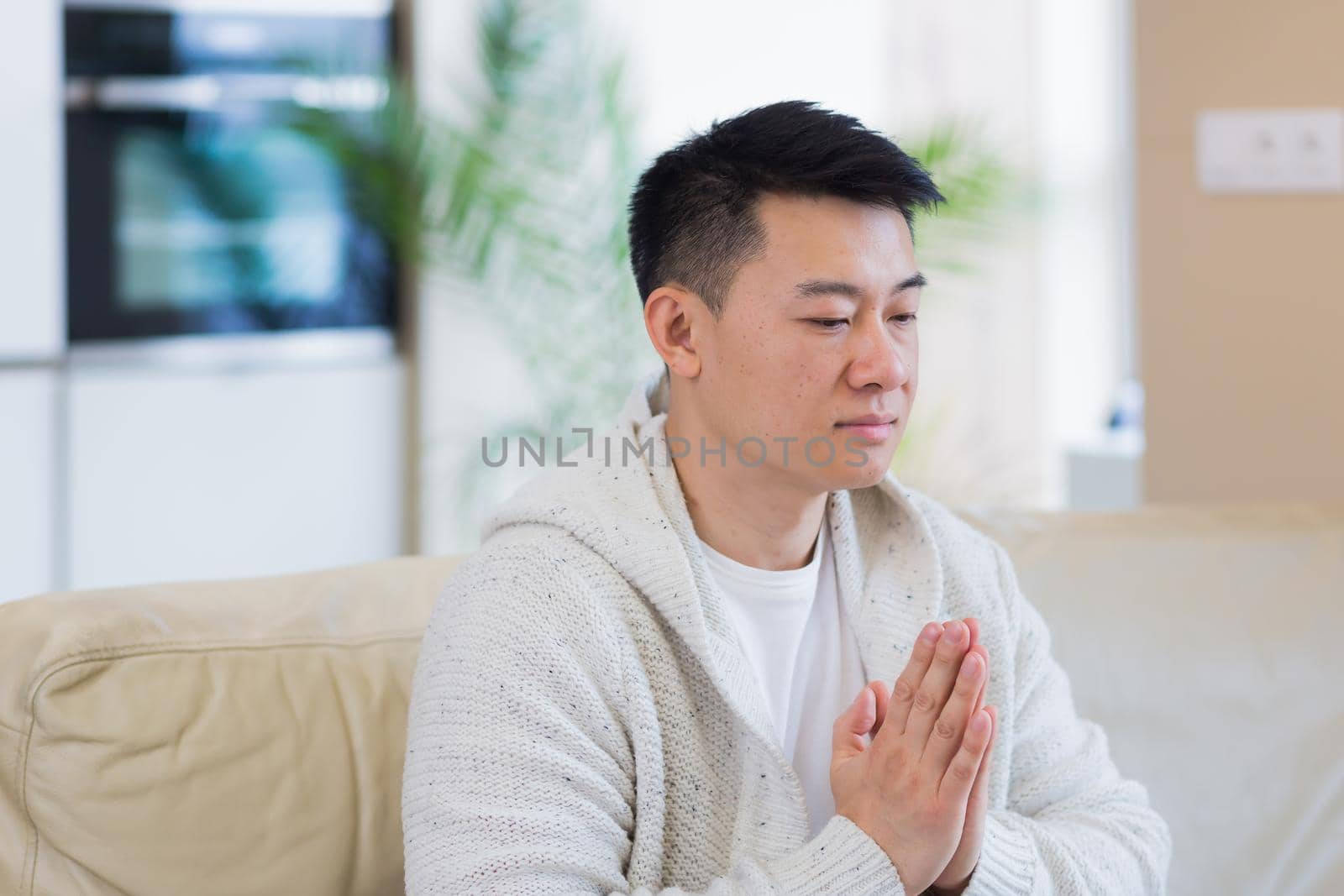 young asian man praying at home alone. Male folding pencil arms and meditating in apartment room. Christian religion traditional spiritual for their hope and believed god forgievness at house
