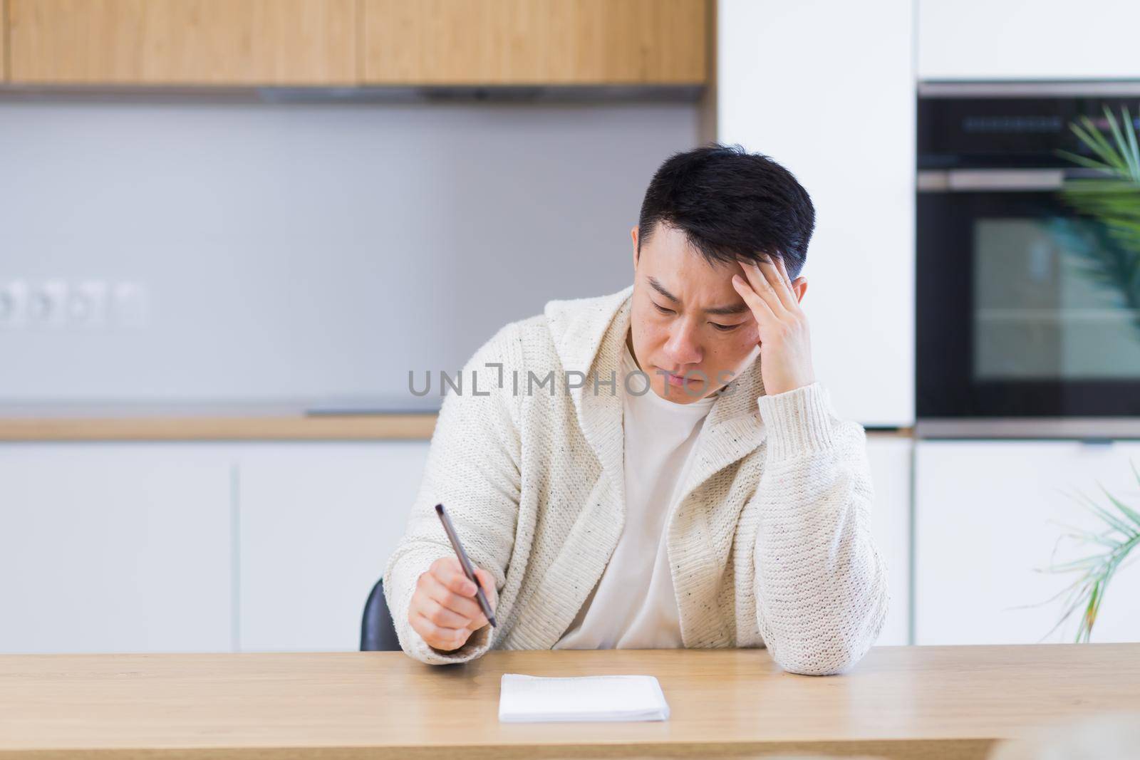 Thoughtful serious young asian man looking away. student writer sit at home office desk with laptop thinking of inspiration search solution ideas lost in thoughts dreaming solving financial problems