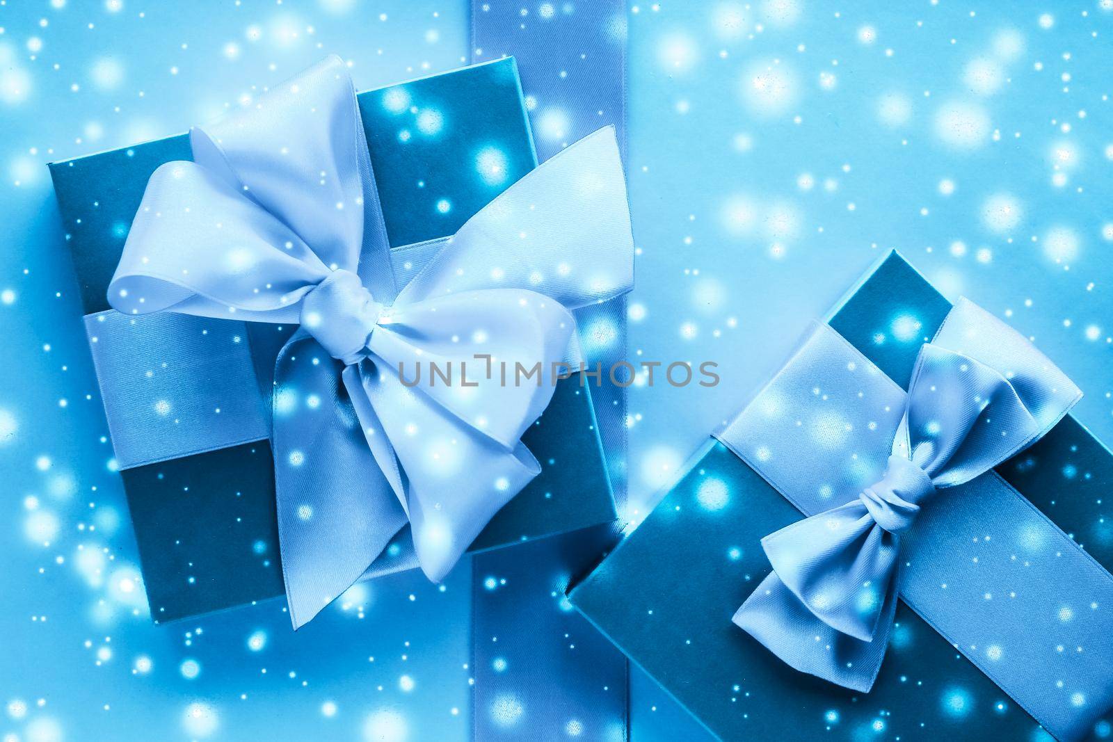 Winter holiday gifts and glowing snow on frozen blue background, Christmas presents surprise by Anneleven