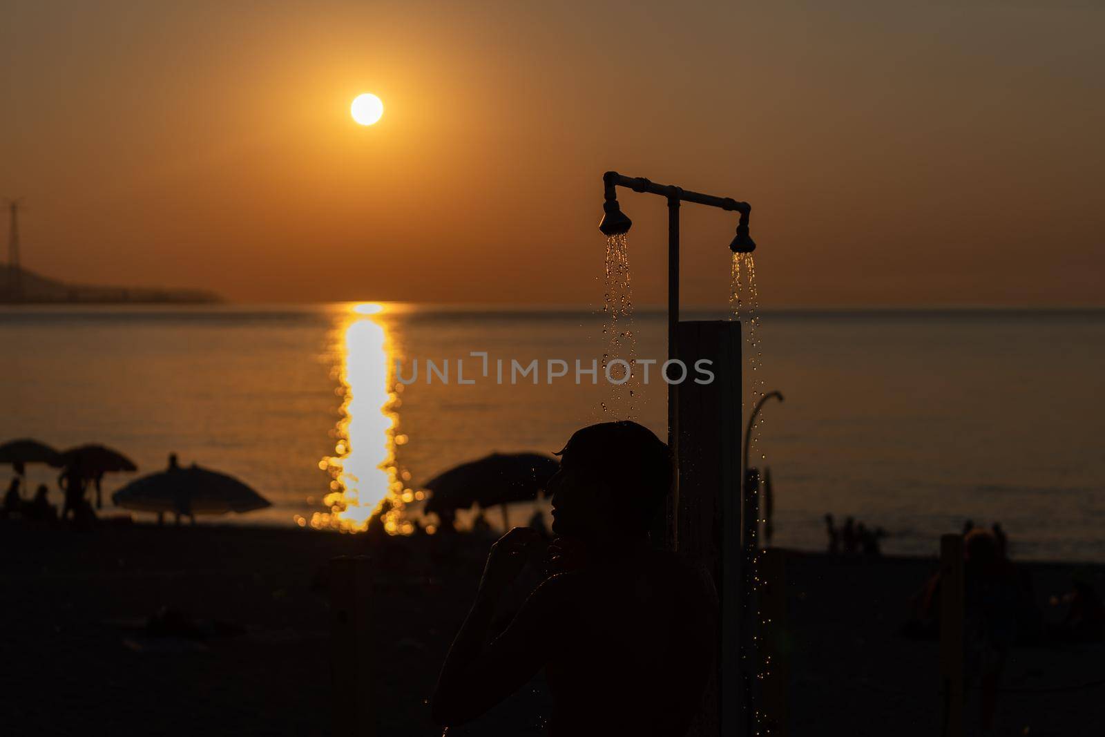 Man silhouette taking shower after swimming at the sea beach. Beautiful view of orange sunset seascape. Summer resort by photolime