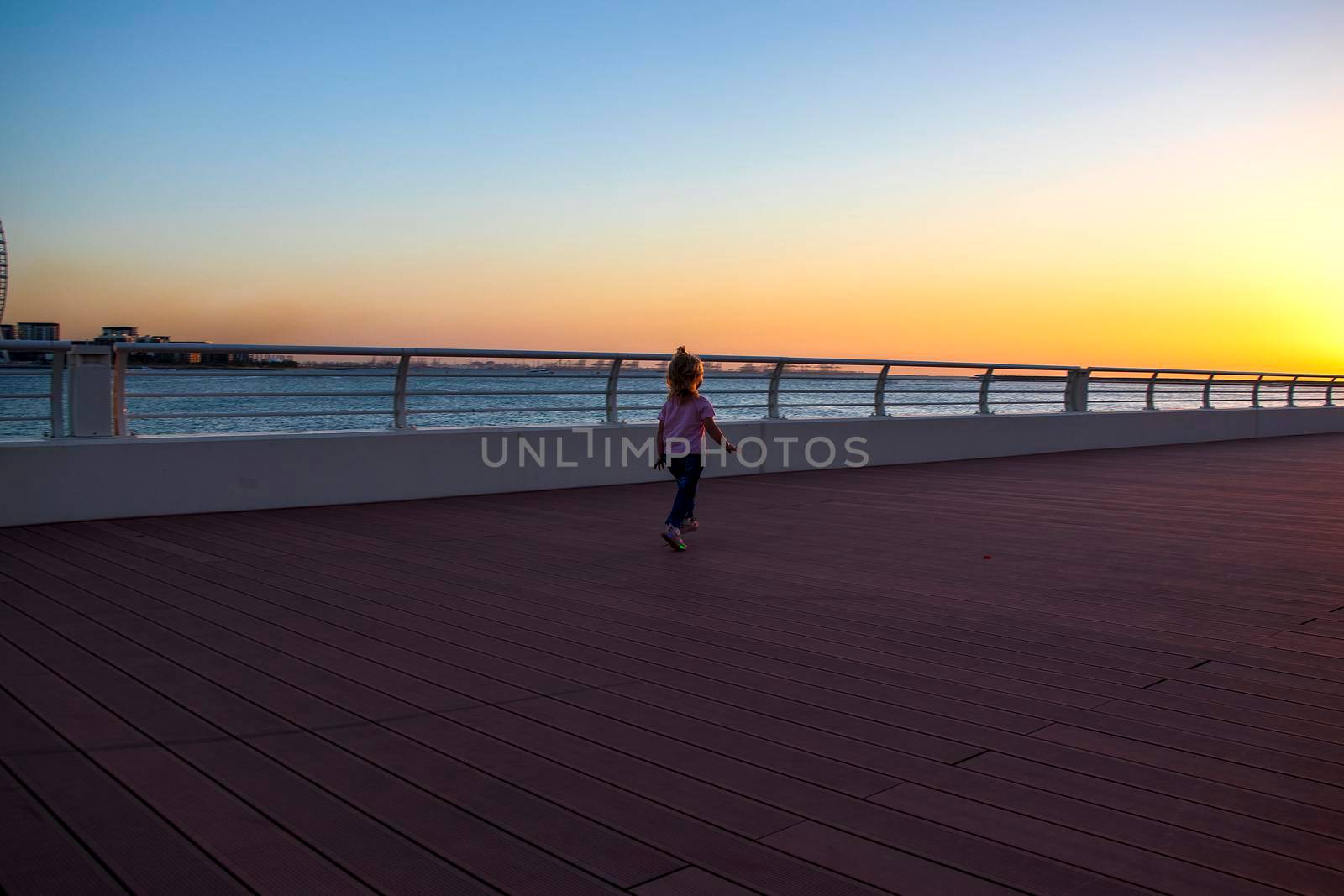 Little girl running on the boardwalk during sunset hour. by pazemin