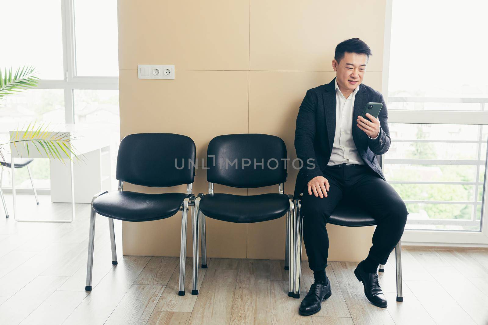 Male asian businessman got good news, rejoices in the waiting room for an interview, near the reception of a modern business center