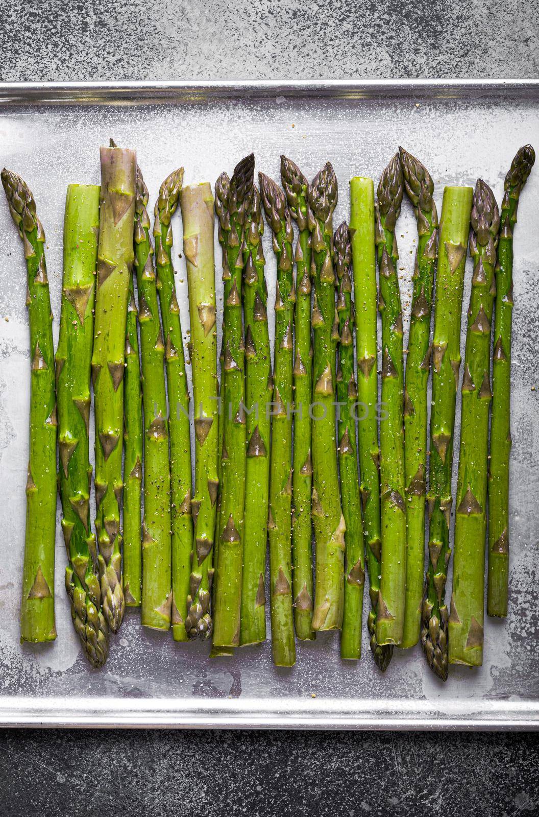 Close-up of fresh green asparagus. Organic asparagus ready for cooking on baking tray sprinkled with olive oil and seasonings, good for healthy dieting, top view, close up.