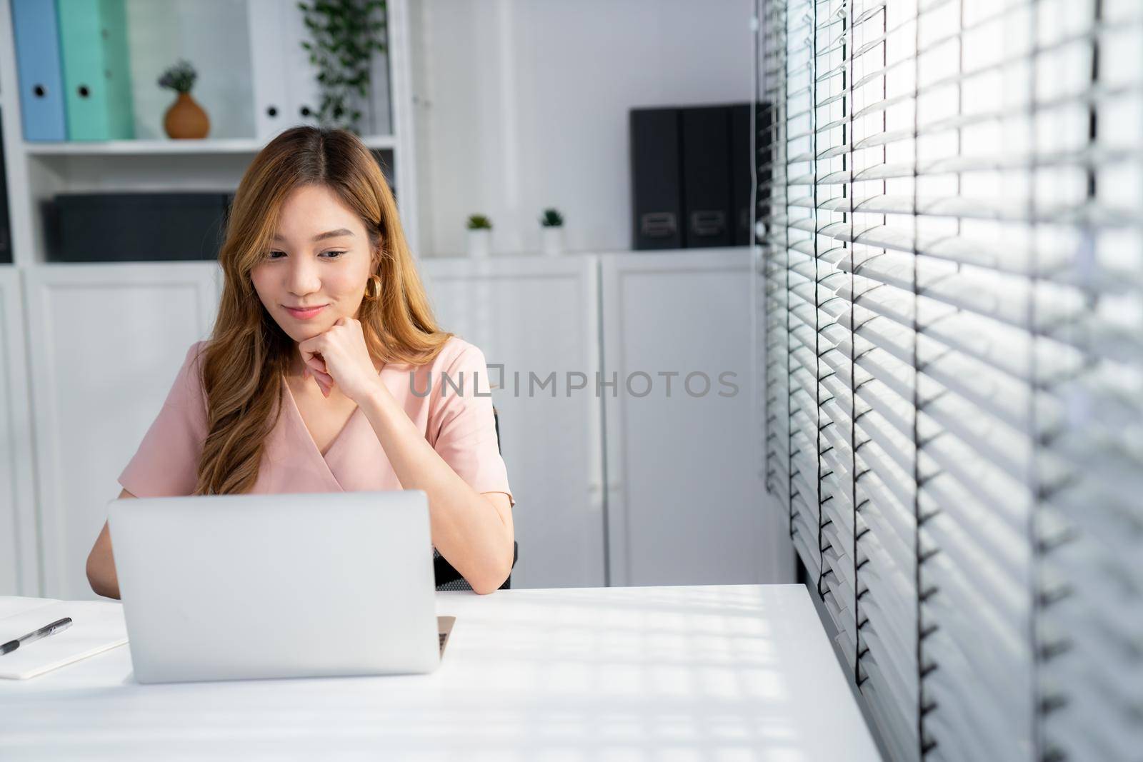 A young Asian female employee sitting at her desk in her office, sitting at desktop in workstation.