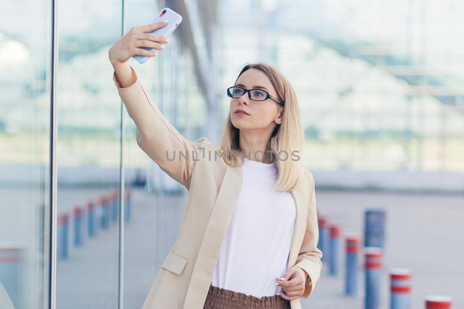 woman wearing glasses blonde holding a mobile phone takes a selfie photo