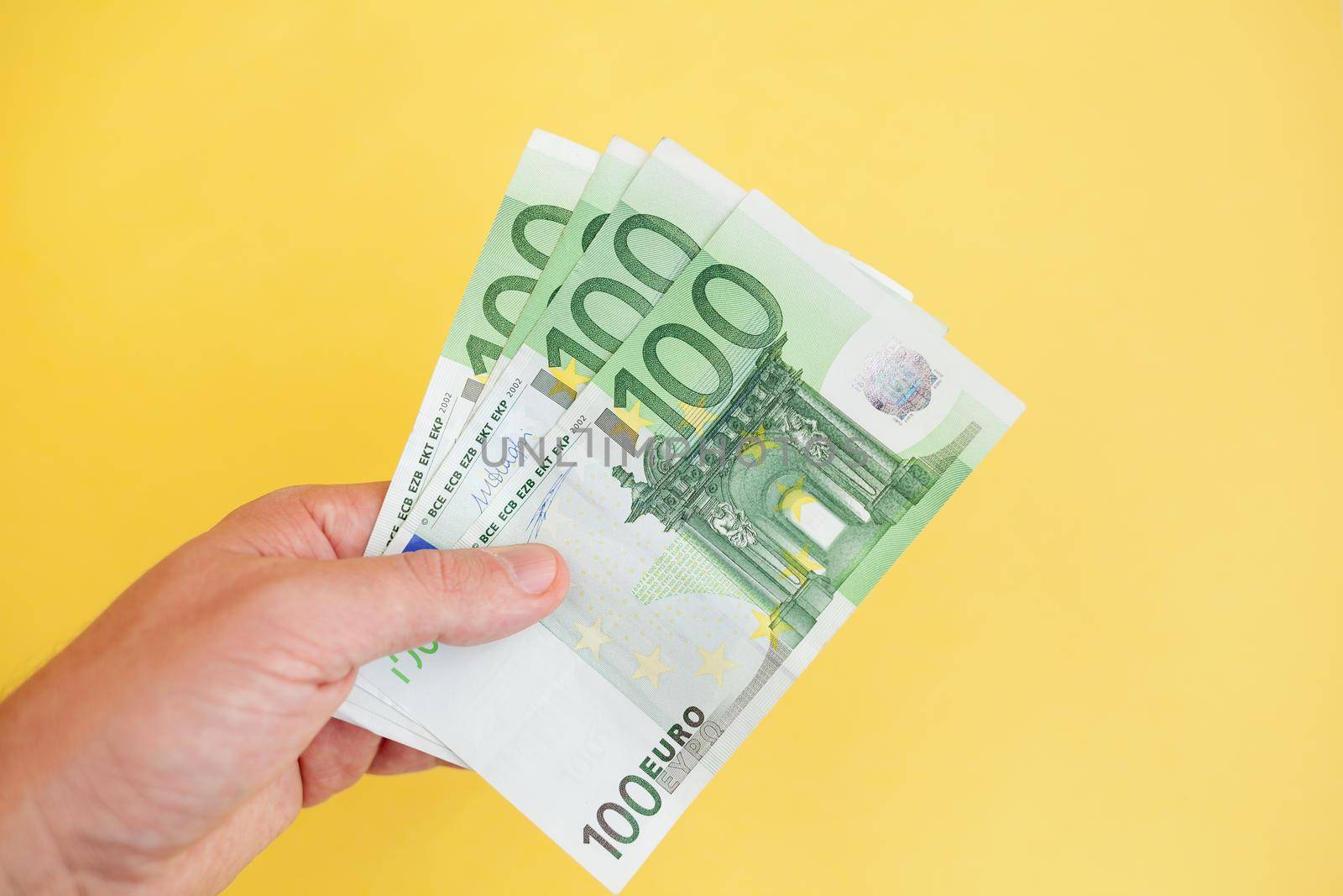 A man holds 100 euro banknotes in his hand on a yellow background. cash paper currency, payment, earning and savings, money and finance concept. Empty space for text