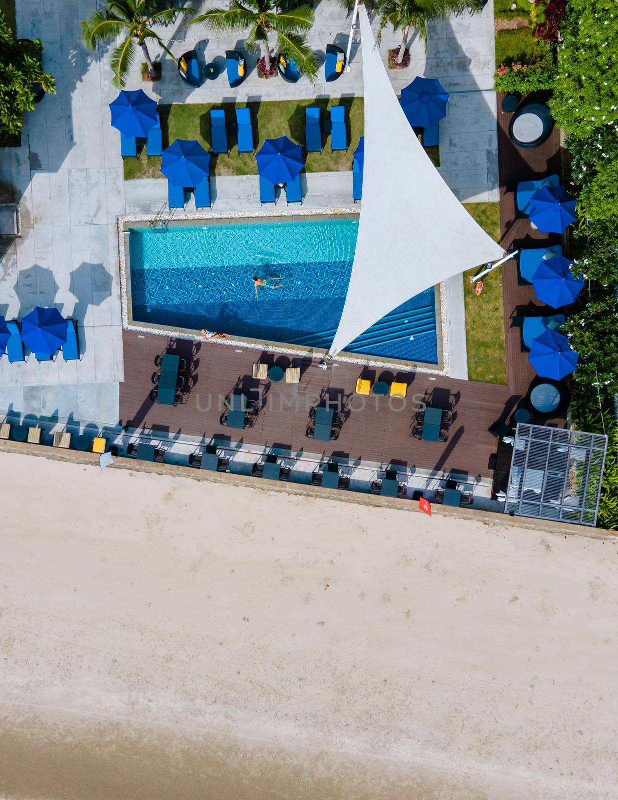 Aerial view from above at pool, tropical swimming pool from above with a drone. Men and women relaxing at a luxury pool during a honeymoon