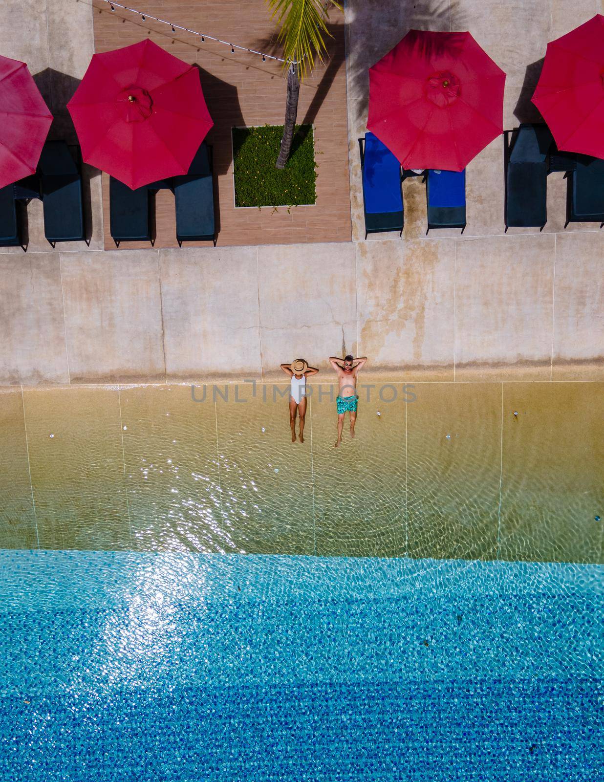 Aerial view from above at pool, tropical swimming pool from above with a drone. Men and women relaxing at a luxury pool during a honeymoon