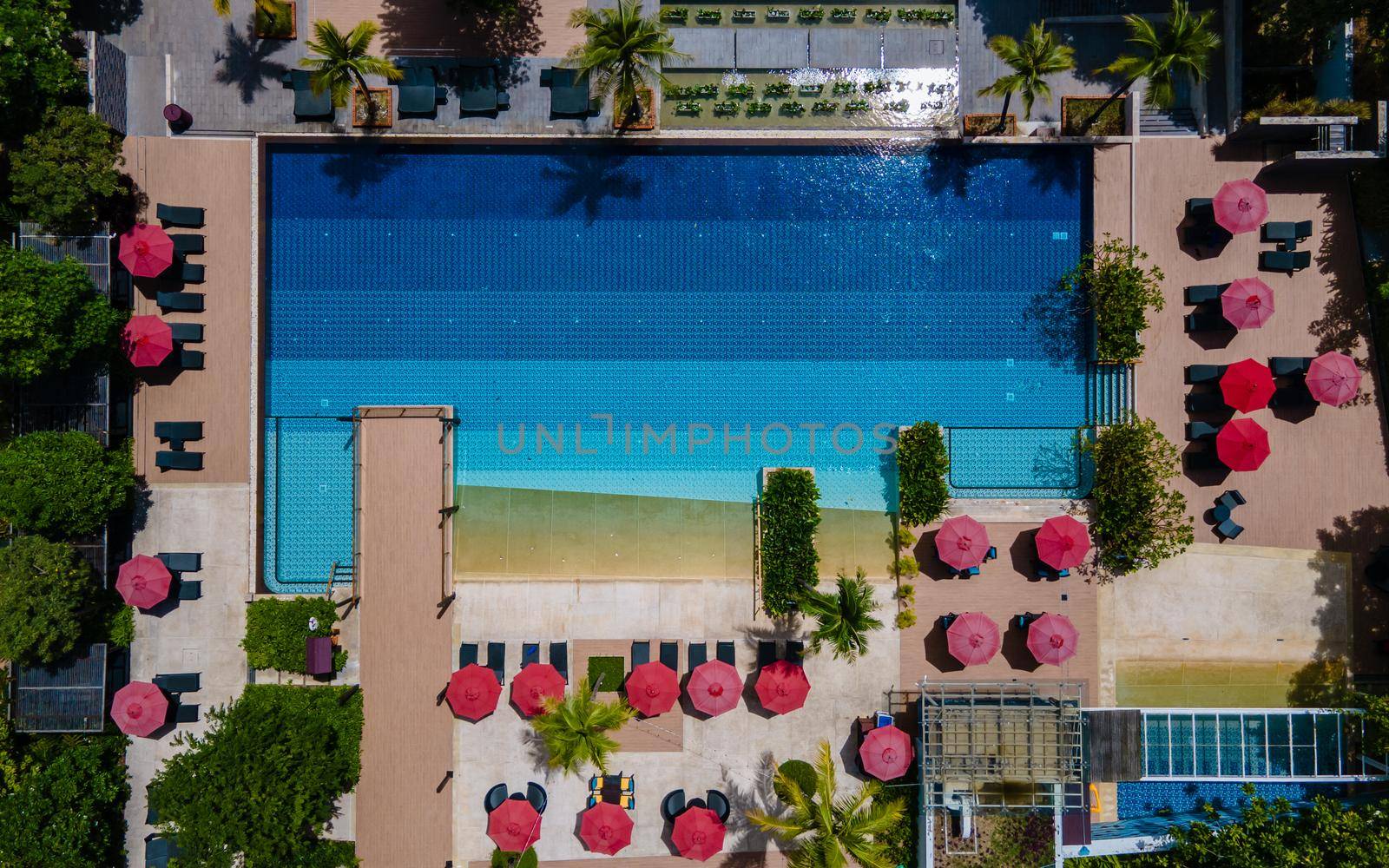 Aerial view from above at pool, tropical swimming pool from above with a drone. Men and women relaxing at a luxury pool during a honeymoon