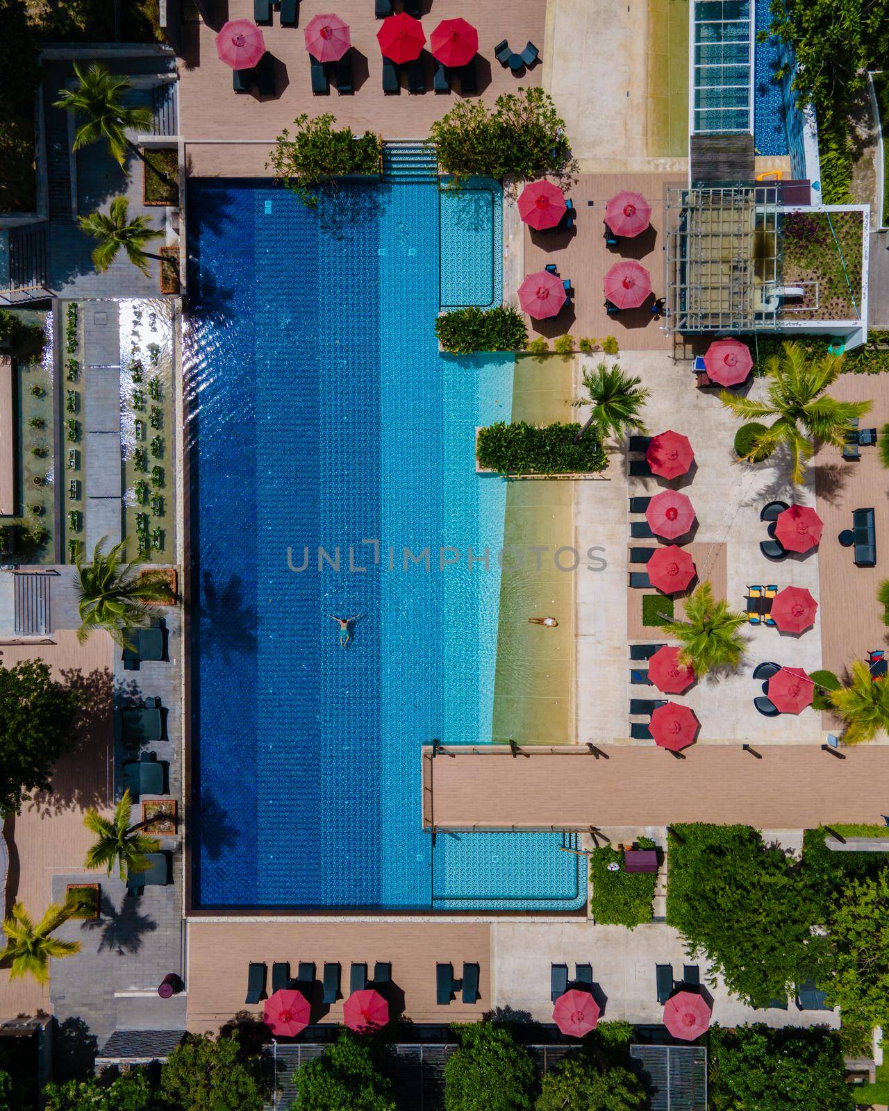 Aerial view from above at pool, tropical swimming pool from above with a drone. Men and women relaxing at a luxury pool during a honeymoon