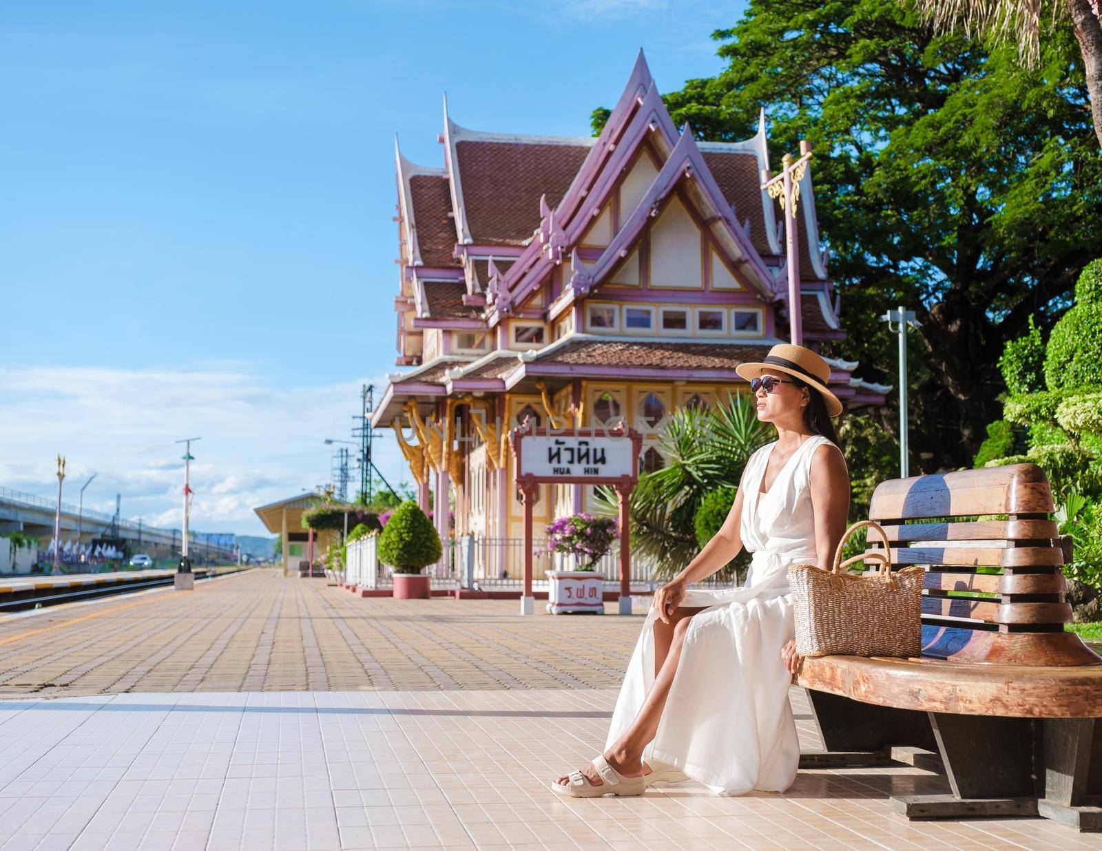 Asian woman with a hat and bag waiting for the train at Hua Hin train station in Thailand.