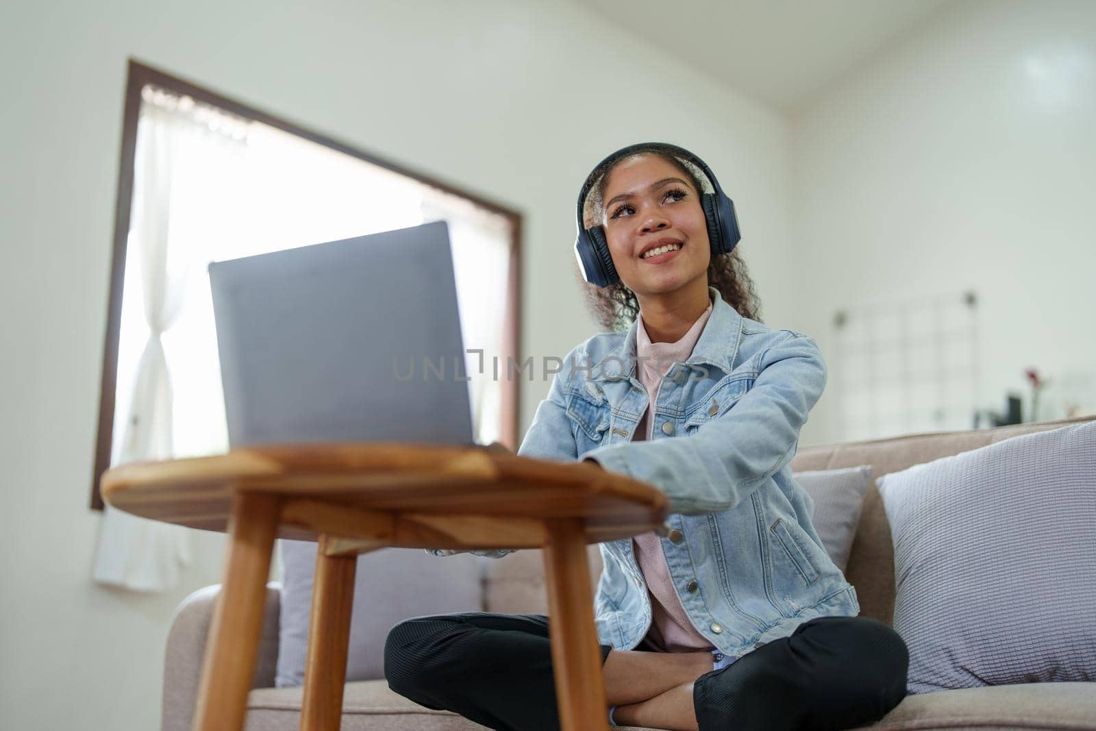 Portrait of an African American sitting on the sofa wearing on-ear headphones and using a computer at home.