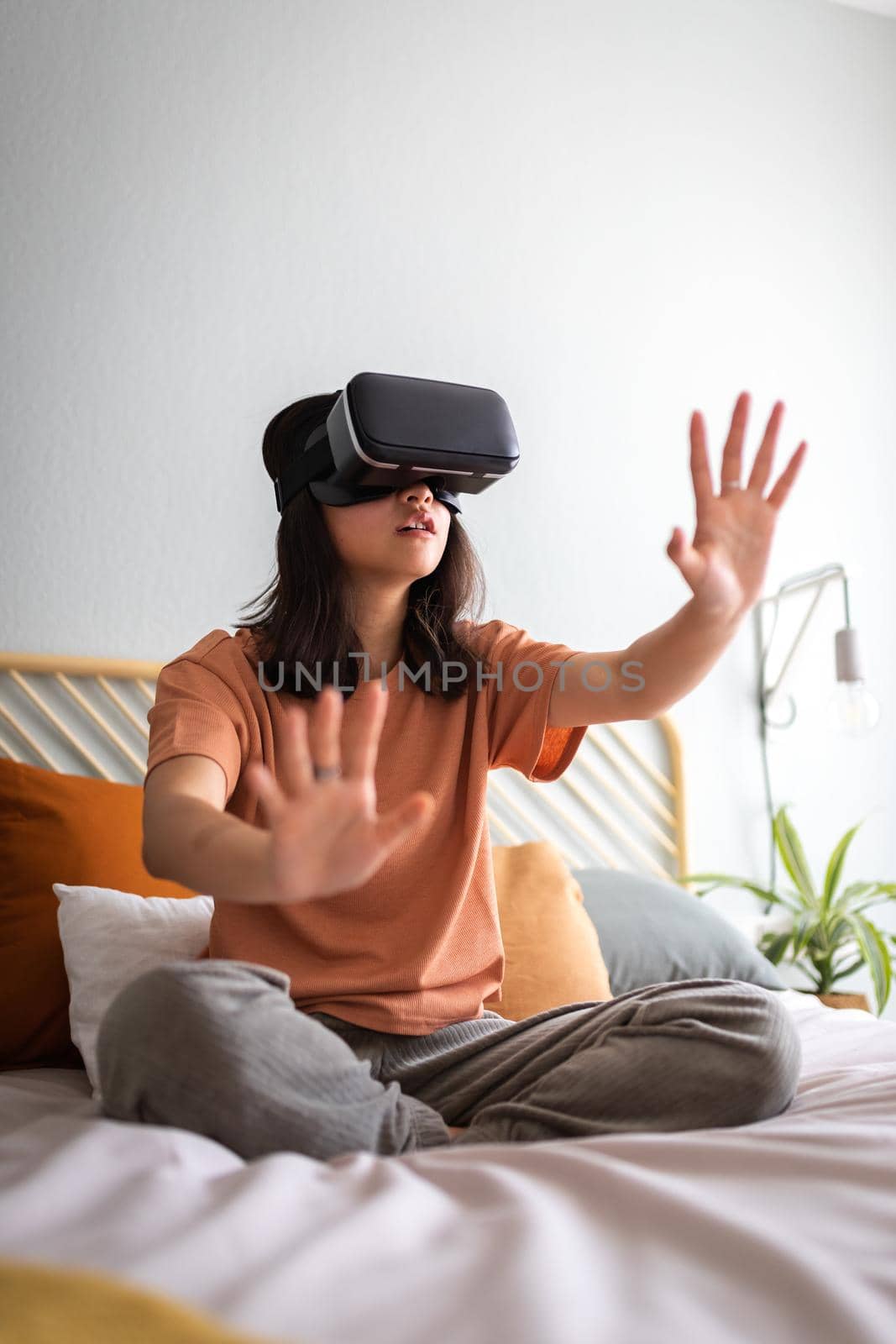 Vertical portrait of teen asian girl moving hands touching objects in 3D world using VR glasses at home. Copy space. by Hoverstock