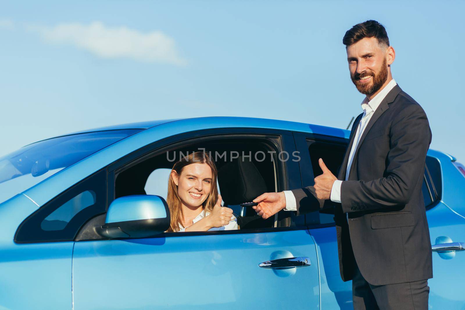 The male car salesman hands over the keys to the female buyer, the purchase agreement is successfully completed